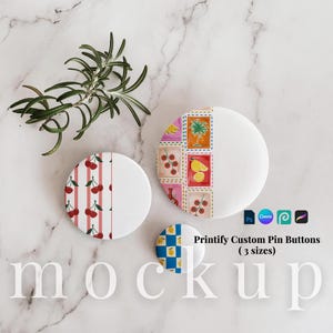 May include: Three round pin buttons in different sizes featuring various designs. One button has a red cherry pattern on white stripes, another displays colorful food and plant illustrations in squares, and the smallest has a blue and yellow checkerboard.