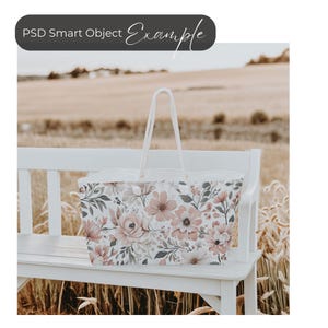 May include: A white tote bag with a floral print featuring pink, gray, and white flowers. The bag is sitting on a white bench.