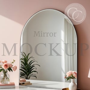 May include: A white arched mirror with a black frame, sitting on a white vanity table. The mirror is reflecting a pink wall, a white curtain, and a green plant. The text "Mirror Mockup" is visible in the reflection.