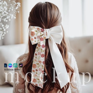 May include: A white satin ribbon bow with a floral print. The bow is tied in the hair of a person with long brown hair.