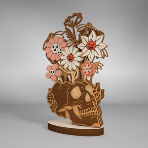 May include: A wooden skull sculpture with a bouquet of pink and white flowers with jack-o-lantern faces. The flowers are arranged in the skull's eye sockets.
