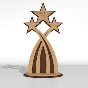 May include: A wooden trophy featuring three star-shaped toppers atop curved, intersecting supports on a circular base. The central star is engraved with the text Edward Norton and the year 2026. The design uses light and dark brown wood tones.