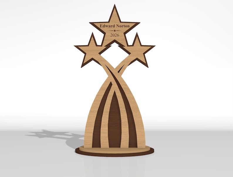 May include: A wooden trophy featuring three star-shaped toppers atop curved, intersecting supports on a circular base. The central star is engraved with the text Edward Norton and the year 2026. The design uses light and dark brown wood tones.
