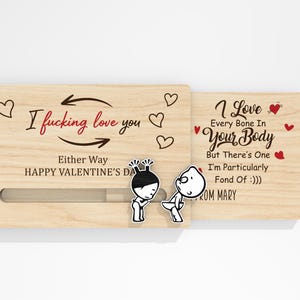 May include: A wooden Valentine's Day card with the text "I fucking love you" and "I love every bone in your body". The card features cartoon figures and heart illustrations. The card is light brown.