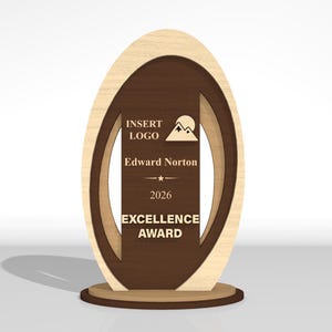 May include: An oval-shaped wooden award plaque featuring a light wood outer frame and a dark brown center panel. The center panel displays the text INSERT LOGO, a mountain icon, Edward Norton, 2026, and EXCELLENCE AWARD in light-colored lettering.