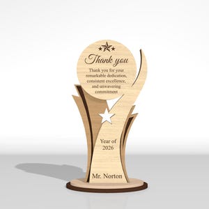 May include: A light-colored wooden trophy with a circular top featuring a star and the text Thank you for your remarkable dedication, consistent excellence, and unwavering commitment. Below is a star cutout, Year of 2026, and Mr. Norton.