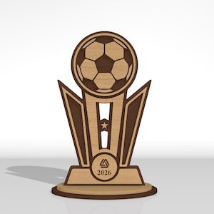 May include: A laser-cut wooden trophy featuring a soccer ball at the top, a central column with a star cutout, and a base displaying a triangular logo and the year 2026. The design uses contrasting light and dark wood tones with clean edges.