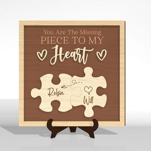Puede incluir: Placa de madera con fondo marr&oacute;n y marco de madera clara. El texto "You Are The Missing Piece To My Heart" est&aacute; encima de dos piezas de rompecabezas. Las piezas del rompecabezas est&aacute;n etiquetadas como "Robin" y "Will".