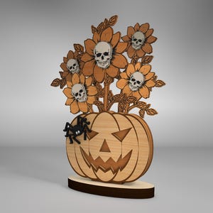 Puede incluir: Decoración de Halloween de madera con una calabaza tallada con una cara espeluznante y un ramo de flores con calaveras en el centro. Una araña negra está posada sobre la calabaza.