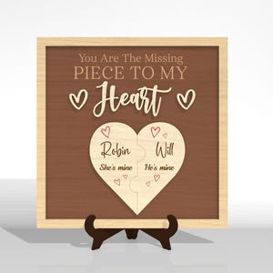Puede incluir: Placa de madera con marco marr&oacute;n claro y fondo marr&oacute;n oscuro. Se muestra el texto "You Are The Missing Piece To My Heart". Un rompecabezas en forma de coraz&oacute;n est&aacute; en el centro, con los nombres "Robin" y "Will" y las frases "She's mine" y "He's mine".