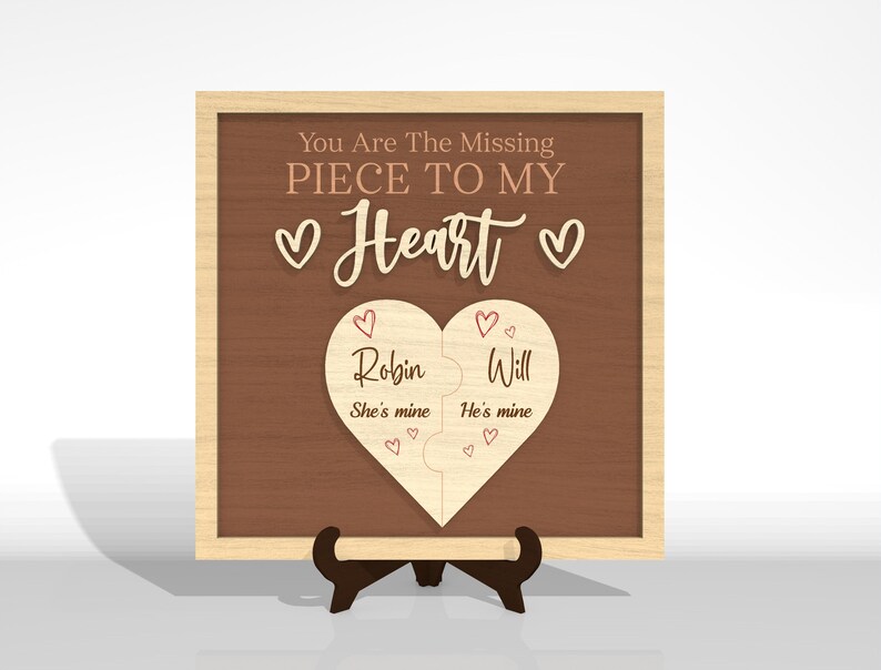 Puede incluir: Placa de madera con marco marr&oacute;n claro y fondo marr&oacute;n oscuro. Se muestra el texto "You Are The Missing Piece To My Heart". Un rompecabezas en forma de coraz&oacute;n est&aacute; en el centro, con los nombres "Robin" y "Will" y las frases "She's mine" y "He's mine".