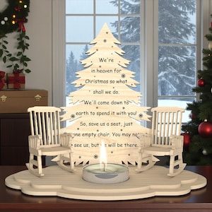 May include: A wooden Christmas tree-shaped decoration with the text "We're in heaven for Christmas so what shall we do." Two small rocking chairs flank the tree, with a lit candle in front. The scene is set in front of a window with a Christmas tree.