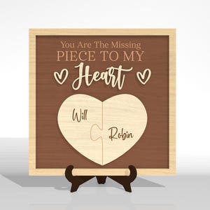 Puede incluir: Rompecabezas de madera en forma de coraz&oacute;n con las palabras "You Are The Missing Piece To My Heart" y los nombres "Will" y "Robin". El rompecabezas se muestra en un marco de madera y se apoya en un peque&ntilde;o soporte.