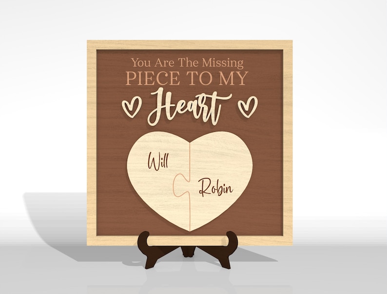 Puede incluir: Rompecabezas de madera en forma de coraz&oacute;n con las palabras "You Are The Missing Piece To My Heart" y los nombres "Will" y "Robin". El rompecabezas se muestra en un marco de madera y se apoya en un peque&ntilde;o soporte.