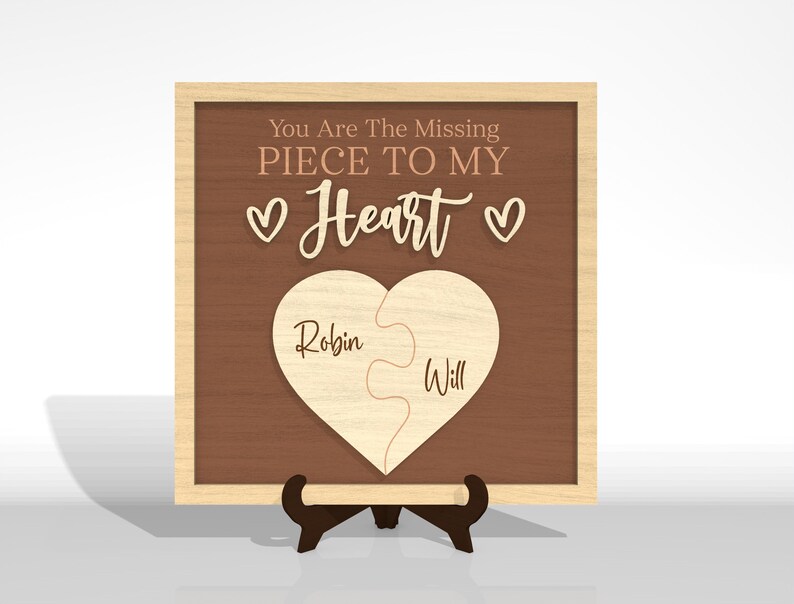 Puede incluir: Placa de madera con fondo marr&oacute;n y marco de madera clara. El texto "You Are The Missing Piece To My Heart" est&aacute; en la parte superior, con un rompecabezas en forma de coraz&oacute;n en el centro. Los nombres "Robin" y "Will" est&aacute;n en las piezas del rompecabezas.