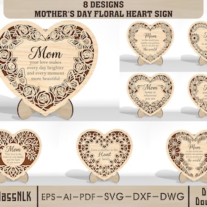 Könnte beinhalten: Holzherzförmige Schilder mit floralen Designs und dem Wort "Mom" in verschiedenen Stilen. Jedes Schild hat eine einzigartige Botschaft, wie z.B. "Deine Liebe macht jeden Tag heller". Die Schilder werden auf Holzständern präsentiert, ideal für den Muttertag.