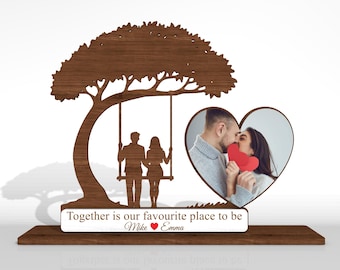 Puede incluir: Un marco de fotos de madera con un diseño de árbol, un columpio con dos siluetas y una foto en forma de corazón. El marco incluye el texto "Together is our favourite place to be" y los nombres "Mike" y "Emma".