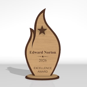 May include: A flame-shaped wooden award plaque featuring a dark brown border and a light wood grain center. It displays a dark brown star at the top and the text Edward Norton, 2026, and EXCELLENCE AWARD engraved in dark brown lettering on the front.