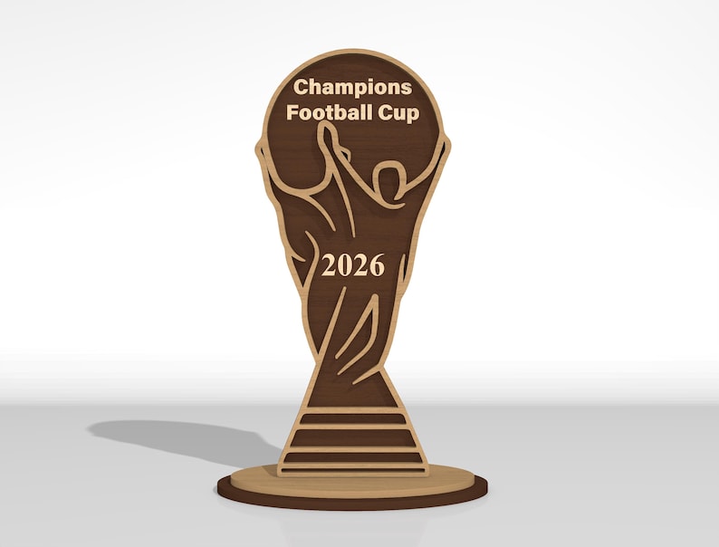 May include: A flat, laser-cut wooden trophy featuring a stylized figure with arms raised, holding a circular top. The text Champions Football Cup is engraved at the top, and the year 2026 is centered on the figure. The design uses layered dark and light wood tones.