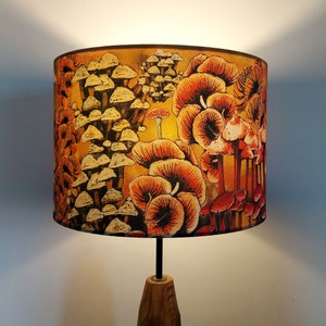 May include: A lampshade with a mushroom design. The lampshade is made of fabric and features a variety of mushrooms in shades of orange, red, and yellow. The mushrooms are arranged in a random pattern on a yellow background.