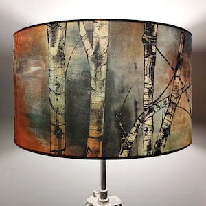 A large lampshade on the top of a chrome standard lamp. The lampshade design shows black and white birch trunks against a mottled background of dark and light greys, with copper/orange tones to the left.