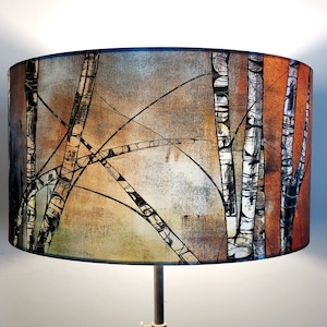 A large lampshade with a silver birch tree design. Five black and white trunks are visible, with criss-crossing black branches creating a semi-abstract pattern. There is a copper orange colour to the right, and pale greys and browns to the left.