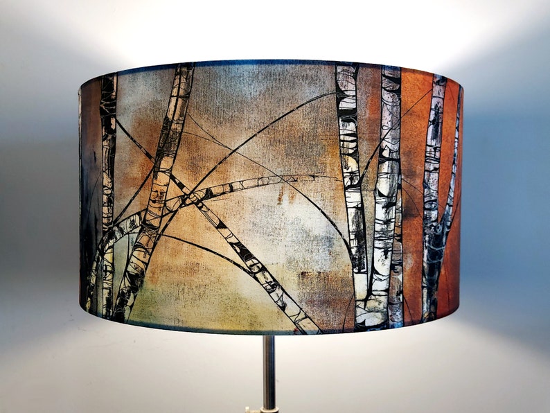 A large lampshade with a silver birch tree design. Five black and white trunks are visible, with criss-crossing black branches creating a semi-abstract pattern. There is a copper orange colour to the right, and pale greys and browns to the left.