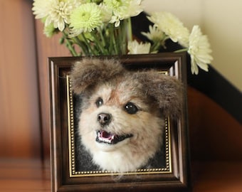 Puede incluir: Un retrato de perro afieltrado enmarcado en un marco de madera marrón. El perro tiene pelaje marrón y canela, ojos negros y una lengua rosada. Un ramo de flores blancas y verdes se encuentra encima del marco.