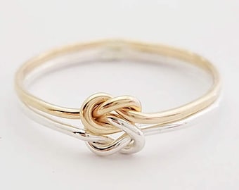 May include: A gold and silver knot ring. The ring is made of two bands of metal that are intertwined to form a knot.
