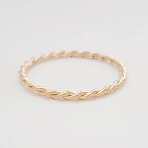 May include: A delicate gold braided ring. The ring is thin and has a simple design.