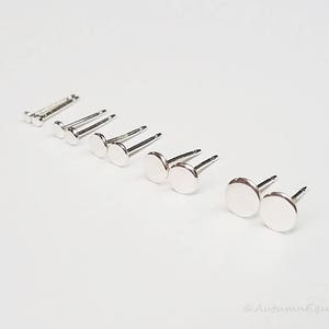 May include: A set of silver stud earrings of varying sizes, arranged in a line on a white surface.