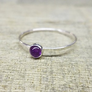 May include: A simple silver ring with a small, round, purple amethyst gemstone.