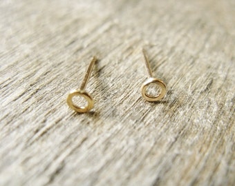 May include: A pair of gold circle stud earrings. The earrings are small and delicate, with a simple design.