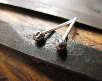 May include: Two silver stud earrings with a hammered ball design. The earrings are shown on a dark metal surface.