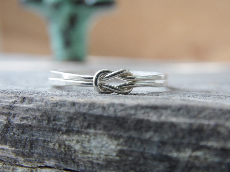May include: A silver knot ring with a simple, elegant design. The ring is made of two strands of wire that are twisted together to form a knot.