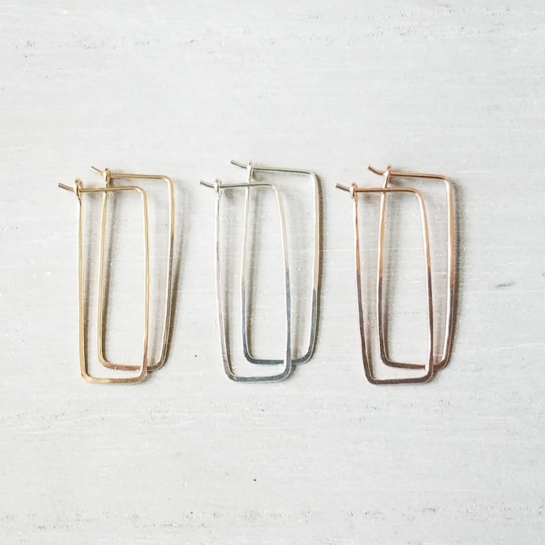 May include: Three pairs of rectangular hoop earrings in gold, silver, and rose gold.