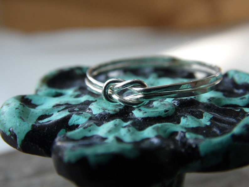 May include: A silver ring with a knot design, resting on a teal and black surface.