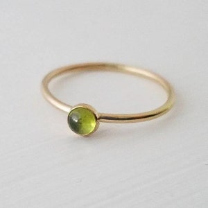 May include: A delicate gold ring with a small, round, green gemstone.