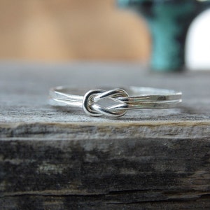May include: A silver ring with a knot design. The ring is simple and elegant, and would make a great gift for a loved one.