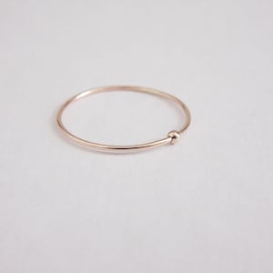 May include: A simple, delicate gold ring with a small bead accent. The ring is made of thin metal and has a smooth, polished finish.