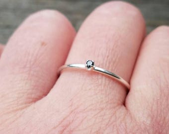May include: A simple silver band ring with a small black gemstone in the center.