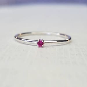May include: A simple silver band ring with a small, bright pink gemstone.