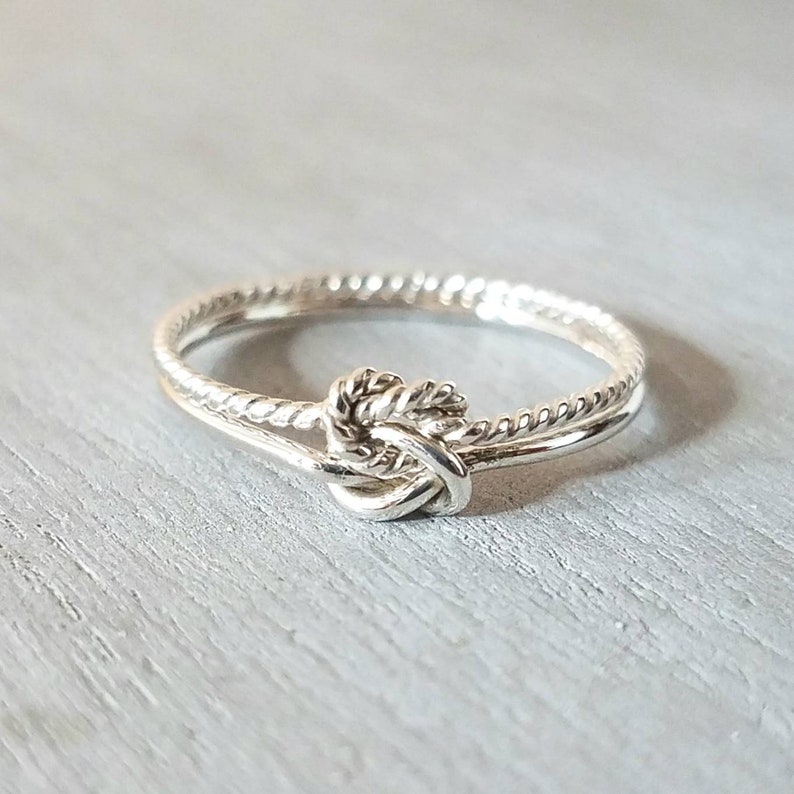 May include: A silver ring with a knot design. The ring is made of two thin bands of twisted metal.