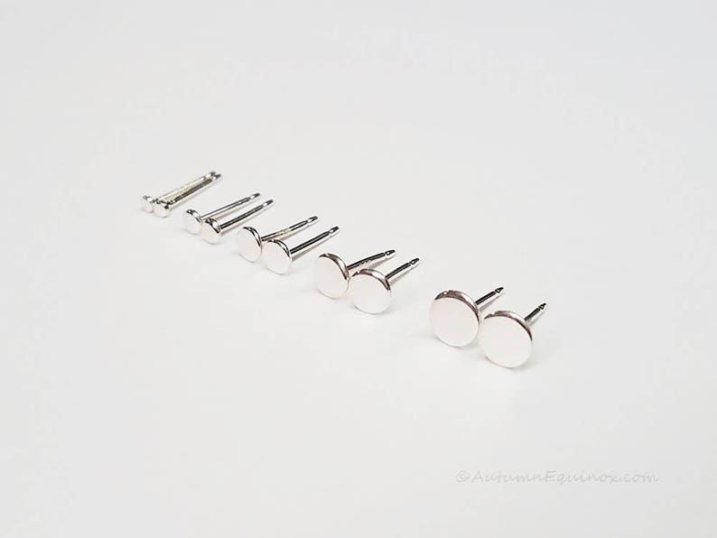 May include: A set of silver stud earrings of varying sizes, arranged in a line on a white surface.