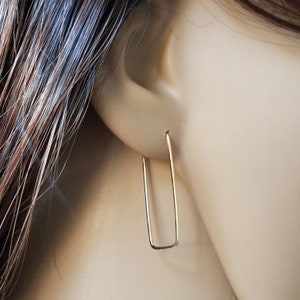 May include: Gold rectangle shaped hoop earrings. The earrings are simple and minimalist.