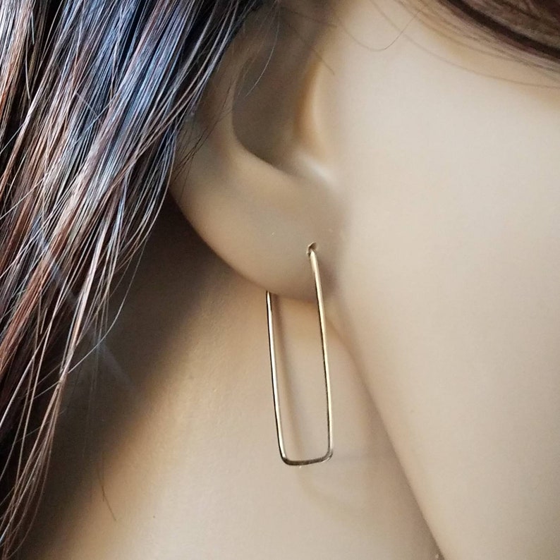 May include: Gold rectangle shaped hoop earrings. The earrings are simple and minimalist.