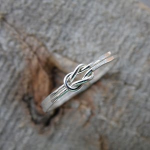 May include: A silver ring with a knot design. The ring is made of two strands of wire that are twisted together to form a knot.