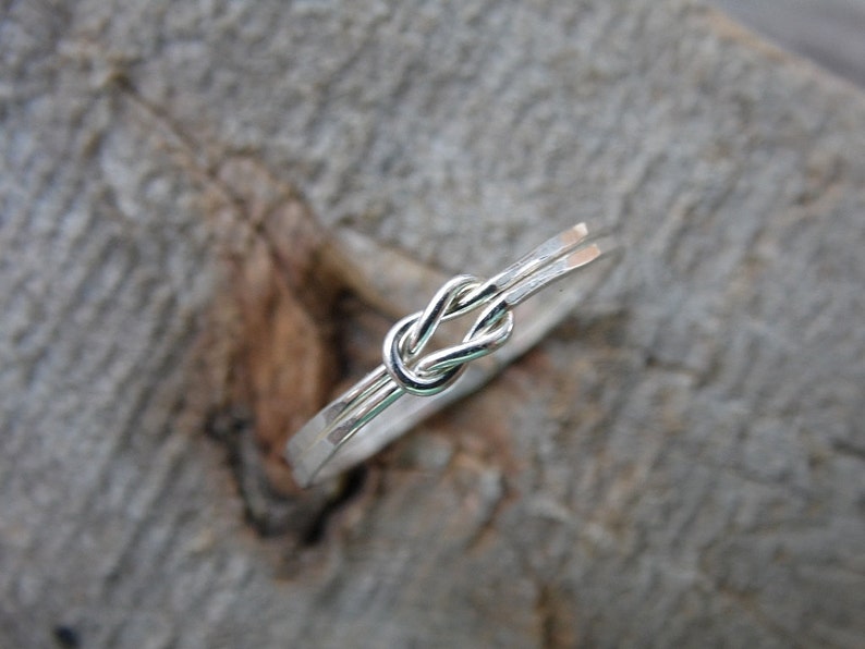 May include: A silver ring with a knot design. The ring is made of two strands of wire that are twisted together to form a knot.