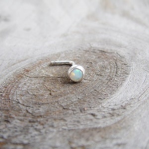May include: A silver nose ring with a small, round, white opal gemstone.