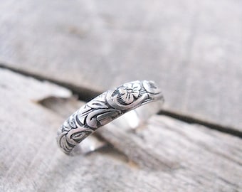 May include: A silver band ring with an intricate floral design. The ring is made of sterling silver and has a polished finish.